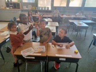 Four first graders smiling at their desks with their project