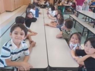 A first grade class smiling at the cafeteria table